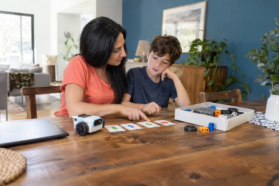 Una madre y su hijo comparan actividades con un robot, tarjetas y piezas.